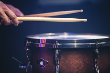 Drummer playing drum sticks on a snare drum on black background.