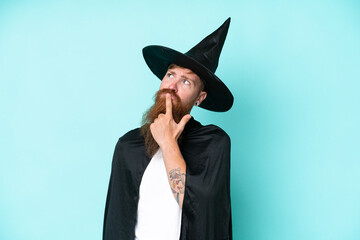 Young wizard in halloween isolated on blue background having doubts while looking up