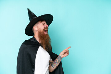 Young wizard in halloween isolated on blue background pointing finger to the side and presenting a...