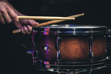 Drummer playing drum sticks on a snare drum on black background.