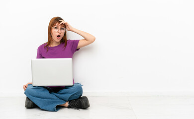 redhead girl with a laptop sitting on the floor doing surprise gesture while looking to the side