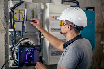 Man, an electrical technician working in a switchboard with fuses, uses a tablet.