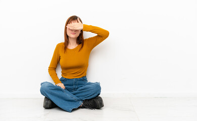 Redhead girl sitting on the floor isolated on white background covering eyes by hands. Do not want to see something