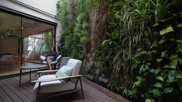 Mujer descansa en un sill&oacute;n mecedora delante de un jard&iacute;n vertical