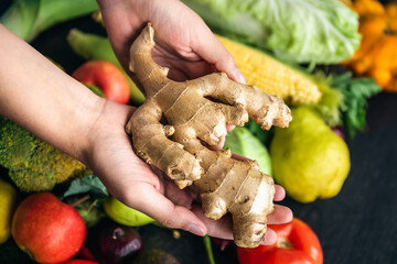 Ginger root in female hands on a blurred background of vegetables, top view.