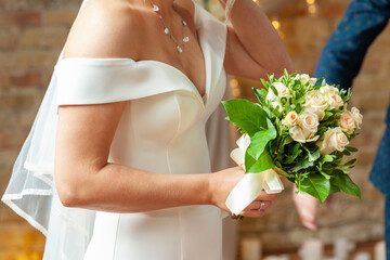 Wedding. The girl in a white dress and a hand of guy at background. Bride holding a beautiful bouquet of white pastel tones flowers and greenery, decorated with silk ribbon.