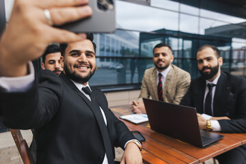 Business people outdoor meeting. Friends business partners take a selfie at a meeting. An international group of men in suits sit at an outdoor table and talking.
