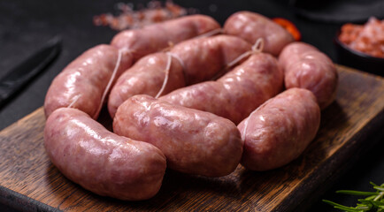 Raw barbecue sausages on a wooden cutting board with spices and herbs