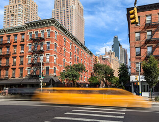 Yellow taxi speeding down the road through the Hell's Kitchen neighborhood of New York City with...