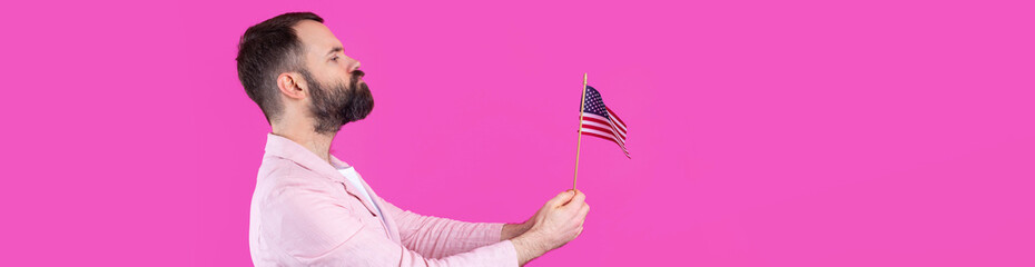 Portrait of a satisfied young man with a beard with an American flag on a red studio background....