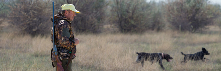 Hunter man in camouflage with a gun during the hunt in search of wild birds or game.