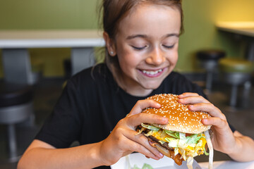 A little girl eats an appetizing burger, close-up.