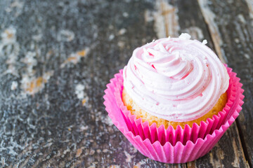 Coconut cupcake with pink curd cream on wooden background