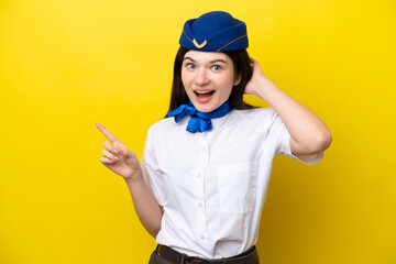 Airplane stewardess Russian woman isolated on yellow background surprised and pointing finger to the side