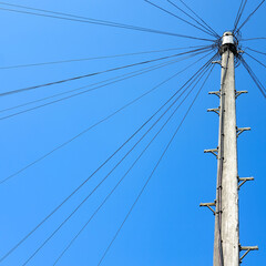 A pole with lots of wires coming out of it in a circular pattern with a bright blue sky as a backdrop.  Image has copy space.