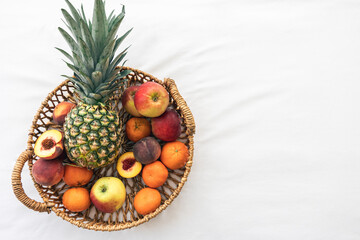 Pineapple and other exotic fruits in a basket on a white background, top view.