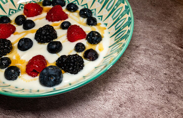 Homemade preparation of dessert with yogurt, strawberries, blueberries and honey. Perspective view from above.