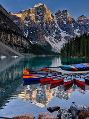 Late sunlight strikes the rugged Canadian Rocky Mountain peaks which surround Moraine Lake in Alberta Province as canoes peacefully float on the water - 531509603