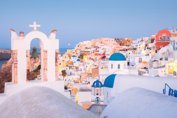 Seaside view at blue hour of traditional white wash buildings and blue dome churches at the popular seaside tourist resort village of Oia on the Greek island of Santorini, Greece. - obrazy, fototapety, plakaty