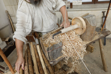 Shallow depth of field (selective focus) details with a craftsman using an ancient Roman woodturning lathe to make a bowl during a historic reenactment event.