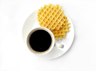 Obraz na płótnie Canvas a cup of fragrant black americano coffee on a white dish with sweet waffles, close up, top view on a white background