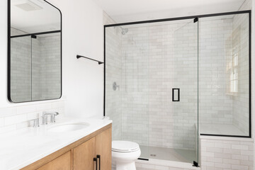 A luxurious bathroom with a wood vanity cabinet and a shower lined with marble subway tiles.