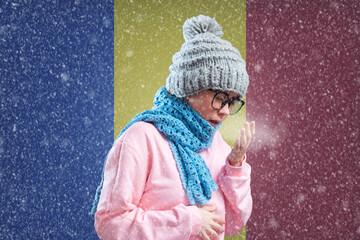 Energy crisis in Europe. Romanian woman in hat and scarf is breathing and coughing. In the background is the flag of Romania. Concept of sanctions, refusal of gas and renewable power