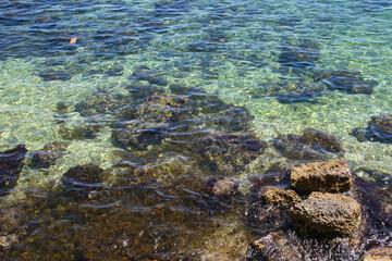 Fototapeta na wymiar A rocky shore with beautiful aqua-marine coloured water off the coast of Sicily, Italy. Image has copy space.