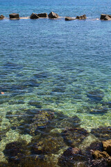 A rocky shore with beautiful aqua-marine coloured water off the coast of Sicily, Italy, with a row of rocks to help stop large waves, known as a breakwater.