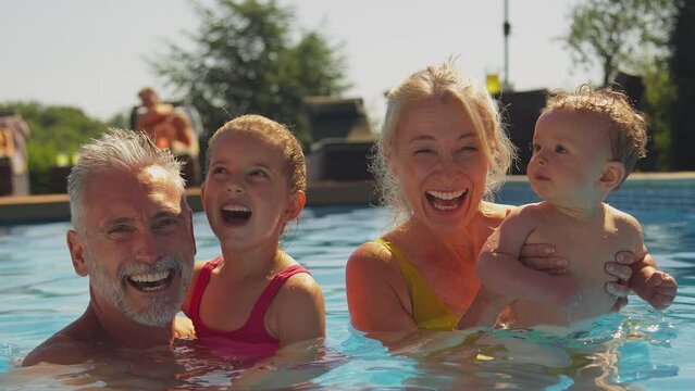 Portrait of smiling grandparents with grandchildren on family summer holiday relaxing and splashing in swimming pool - shot in slow motion
