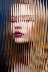 Fashion model behind striped glass, corrugated glass. High fashion effects. Blonde in a red dress, red lipstick. Illusion, special effects, visual object duplication. Blue background 
