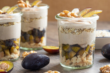 Dessert mit Pflaume, Walnuss, Frischkäse, Joghurt. Quark, Haferflocken, Marmelade und Zimt auf einem Tisch angerichtet