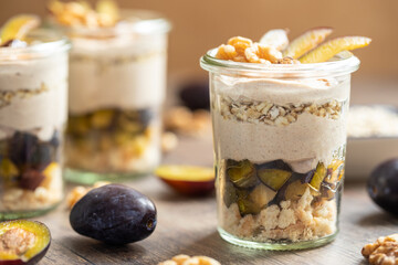 Dessert mit Pflaume, Walnuss, Frischkäse, Joghurt. Quark, Haferflocken, Marmelade und Zimt auf einem Tisch angerichtet