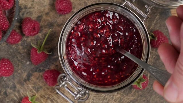 Raspberry jam , marmalade or confiture in a jar with fresh berries. Taking red jam with a spoon. Top view. Sweet food. 4k video