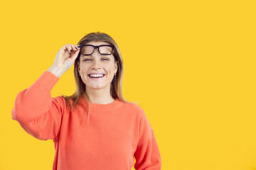 Portrait of smiling girl isolated on yellow studio background take off glasses consider good sale deal or discount. Happy young woman excited with promotion and offer. Copy space, ad.