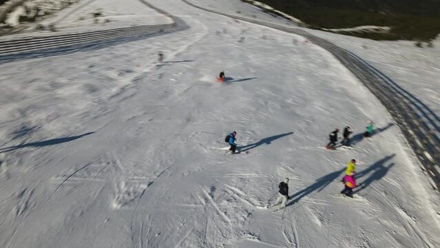 Aerial view with the camera following a person who practices skiing turning from side to side down a hill and kicking up snow in his path