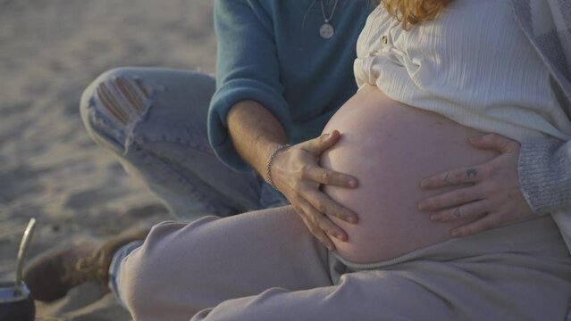 Close-up of unrecognizable pregnant woman with big belly at sunset. Family and future concept