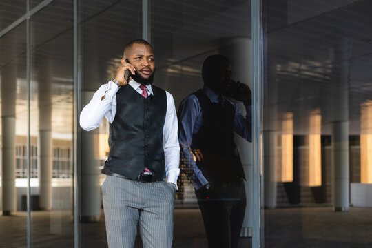 Portrait of handsome afro american businessman using phone in suit against modern building exterior