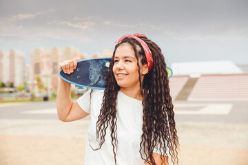 a young woman with dreadlocks holds a skateboard and listens to music.generation z