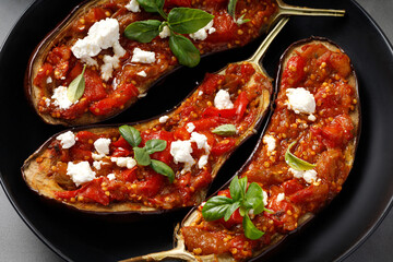 Eggplants stuffed with red sauce, chopped tomatoes, sweet pepper, feta cheese and basil on black...