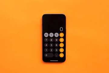 Calculator in phone on orange background. Finance, tax, accounting, statistics and analytical research concept. Top view - obrazy, fototapety, plakaty
