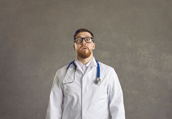 Portrait of a male doctor with a funny surprised and scared expression on a gray background....