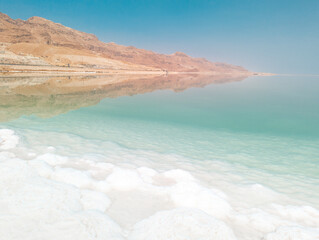 Landscape view on Dead Sea salt crystals formations, clear cyan green water and mountains at Ein Bokek beach, Israel