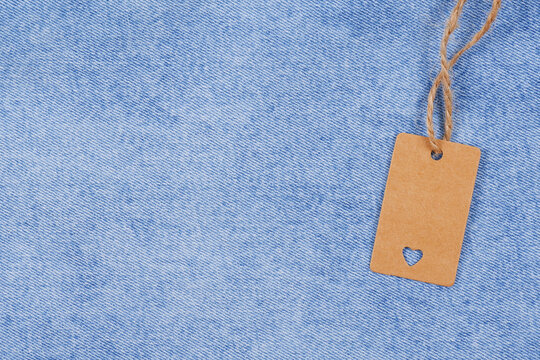 An empty price tag, a gift label template or a kraft paper label with a heart and a jute cord on a blue denim background.Minimalistic shopping concept, Black Friday, sales, denim clothing.Copyspace