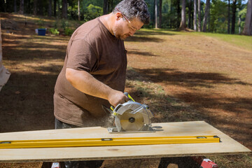 Worker using a circular saw to cut plywood held in his hand