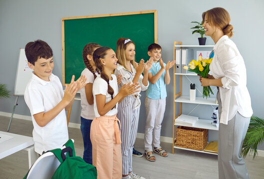 Cheerful schoolchildren in school classroom congratulate their female teacher on International Teacher's Day. Preteen boys and girls give teacher bouquet of flowers and cheerfully applaud her. - Powered by Adobe