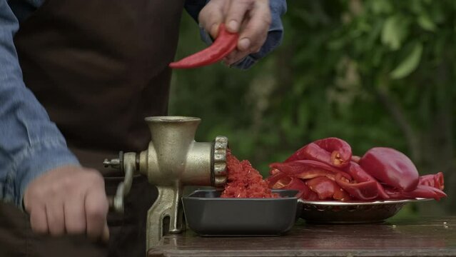 Preparation of homemade sauce with a sweet bell peppers, hot pepper chilli with a grinding machine. Man grinding red peppers on old meat grinder outdoors close-up. Vegetable sauce Healthy organic food