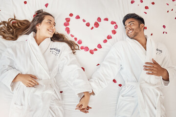 Man and woman married couple on luxury bed celebrate honeymoon, love and relax in romantic vacation spa hotel. Happy, marriage and young people smile on valentines day with rose heart in bedroom