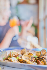 Blurred background with a dish of boiled vongole clams on a table in a cafe, vertical frame, in the background the silhouette of a woman with a glass of wine. Idea for a screensaver or banner
