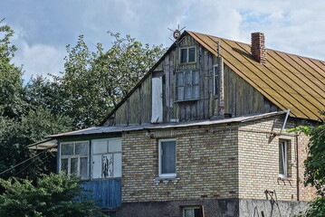 one old rural brown brick house with a wooden attic under a rusty iron roof on the street against the sky